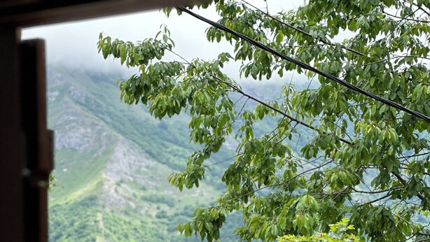 Ein Tisch ist reich gedeckt mit Blumen in einer Vase, Speisen auf Tellern und Gläsern, mit Blick auf eine Berglandschaft.