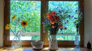 Ein Fenster mit zwei Blumenvasen und einem Korbwägelchen auf einer Holzablage.