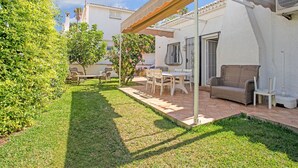 Eine Terrasse mit Gartenmöbeln, einer Pergola und einem weißen Gebäude mit Ziegeldach.