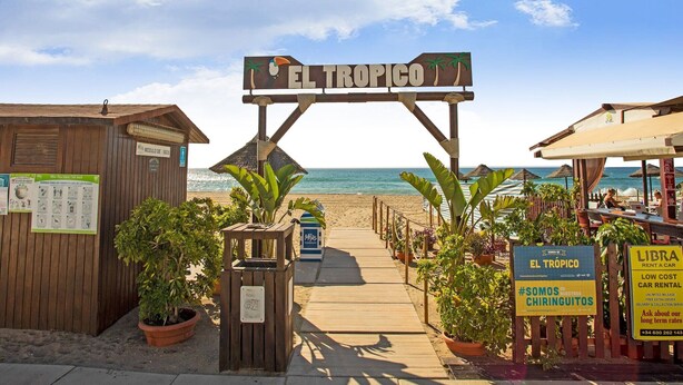 Ein Holzsteg führt zu einem Strandabschnitt, auf einem Schild steht 'EL TROPICO'.