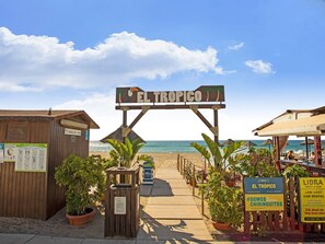 Ein Holzsteg führt zu einem Strandabschnitt, auf einem Schild steht 'EL TROPICO'.