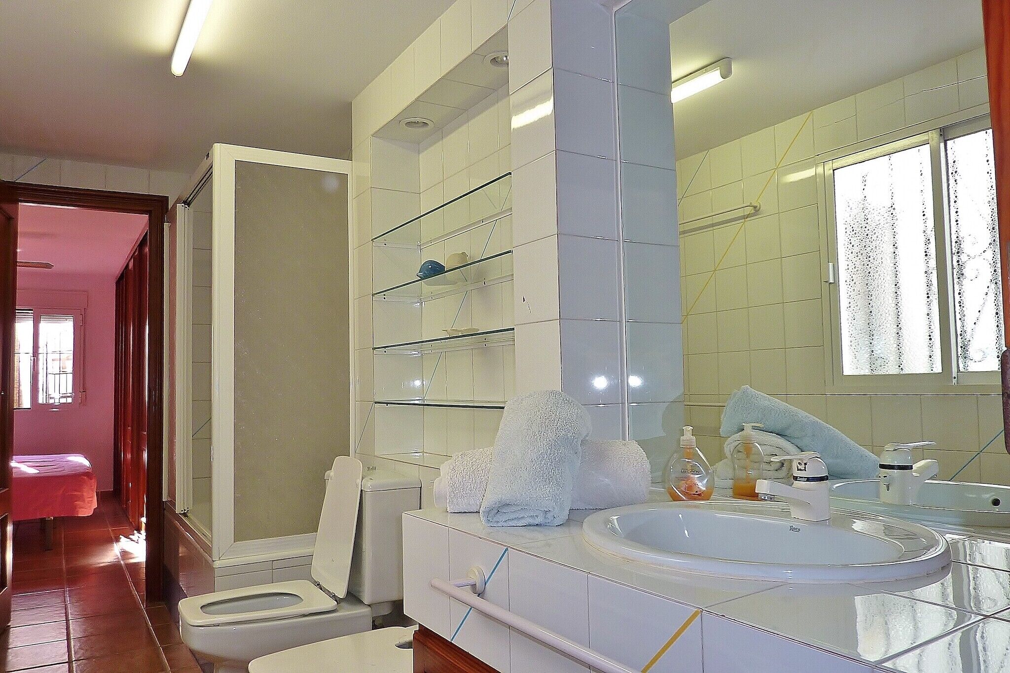Un baño moderno con lavamanos blanco, estantes de vidrio y un espejo grande.