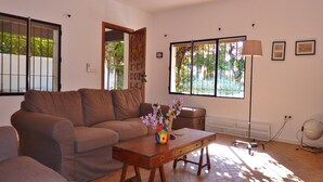A living room with a brown sofa, a wooden coffee table with a vase of flowers, a lamp, and a large window with a view of greenery. - Costa del Sol Villa Near Beach (San Pedro de Alcantara)