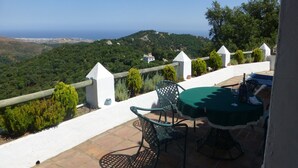 Una terrazza con tavolo e sedie, affacciata su un paesaggio suggestivo con colline e vista mare.
