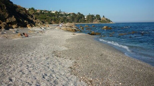 Una spiaggia di ciottoli con affioramenti rocciosi e una vista limpida sul mare.