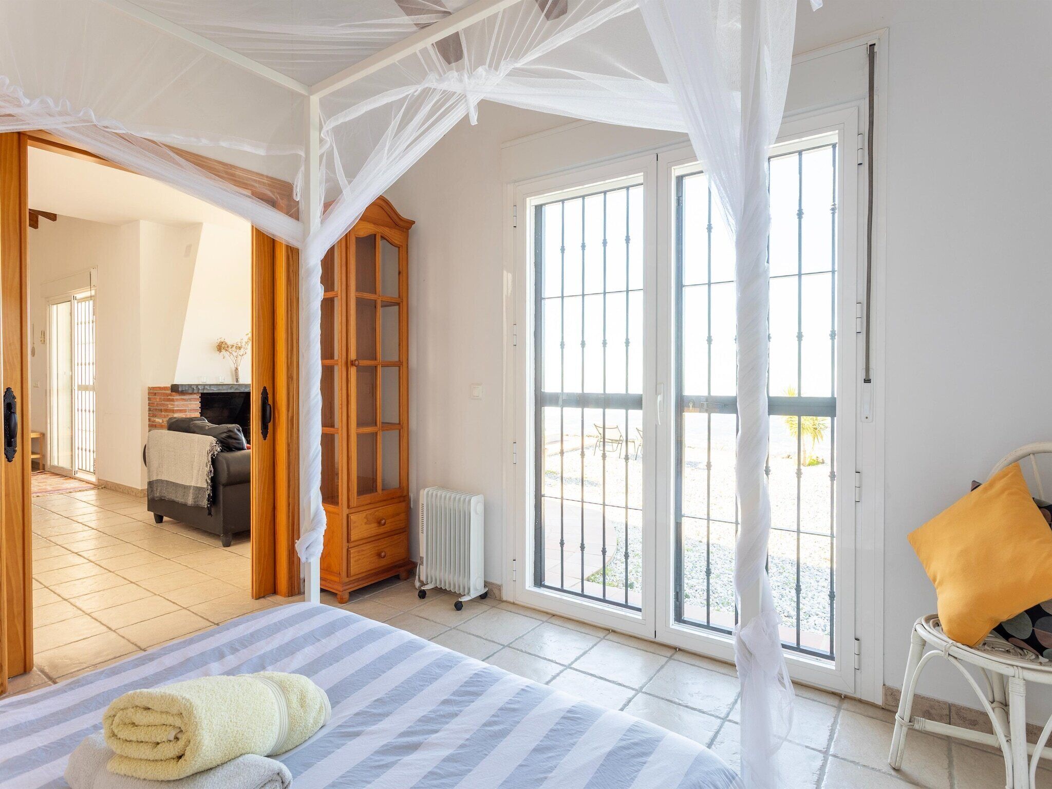 A bedroom with a bed, a wooden wardrobe, a radiator, and a window with a view of the outside.