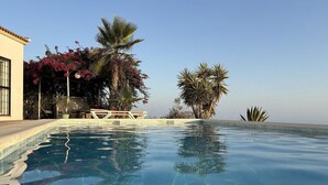 A clear swimming pool with a tiled edge, surrounded by palm trees and a building with a tiled roof. - Villa in Arenas with Sea Views and Private Pool (Arenas)