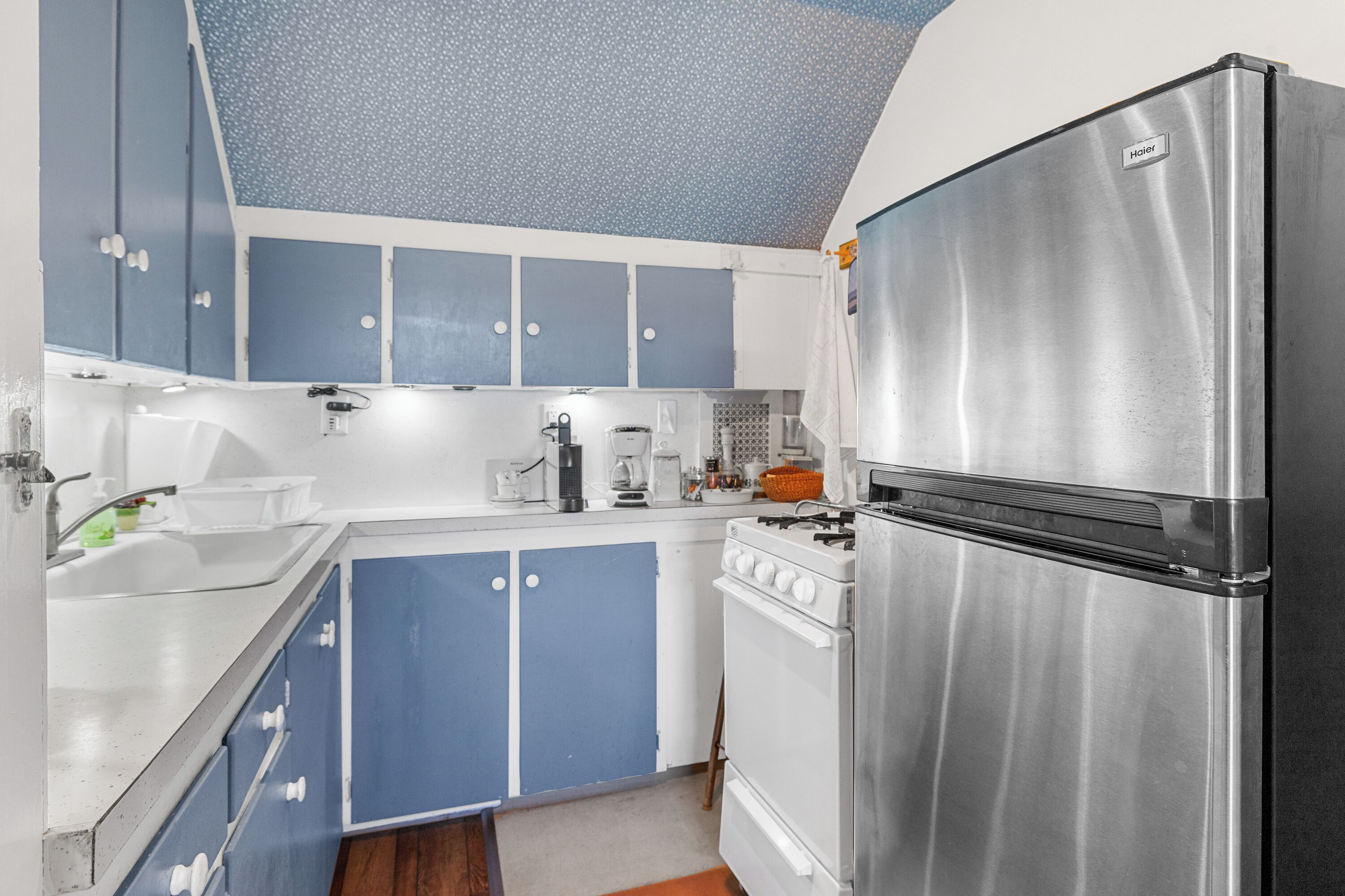 A compact kitchen with blue cabinets, a stainless steel refrigerator, and a white stove.