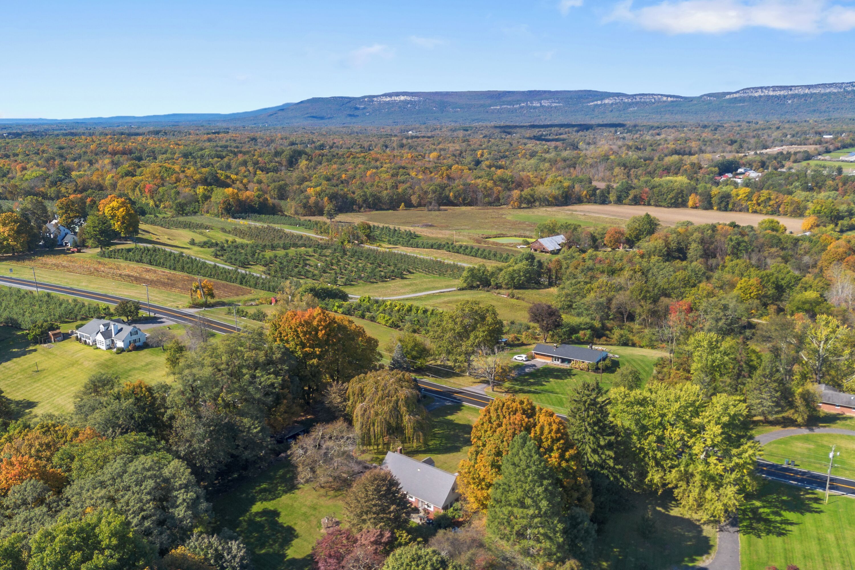 An aerial view of a rural landscape with rolling hills, a road, and scattered houses.