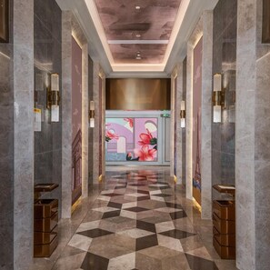 A hallway with a geometric patterned floor, marble walls, and a central wall with a floral mural.