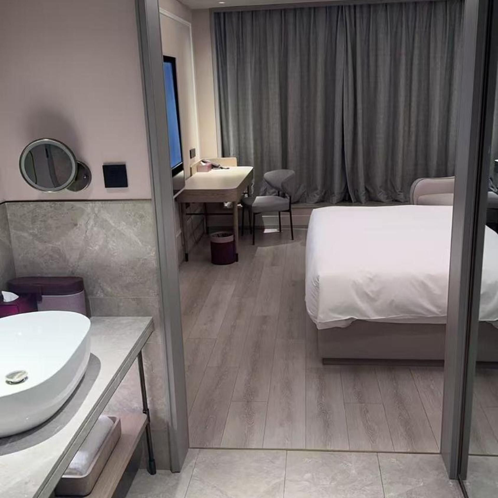 A hotel room with a bed, a desk, a chair, a bathroom with a sink, and a mirror.