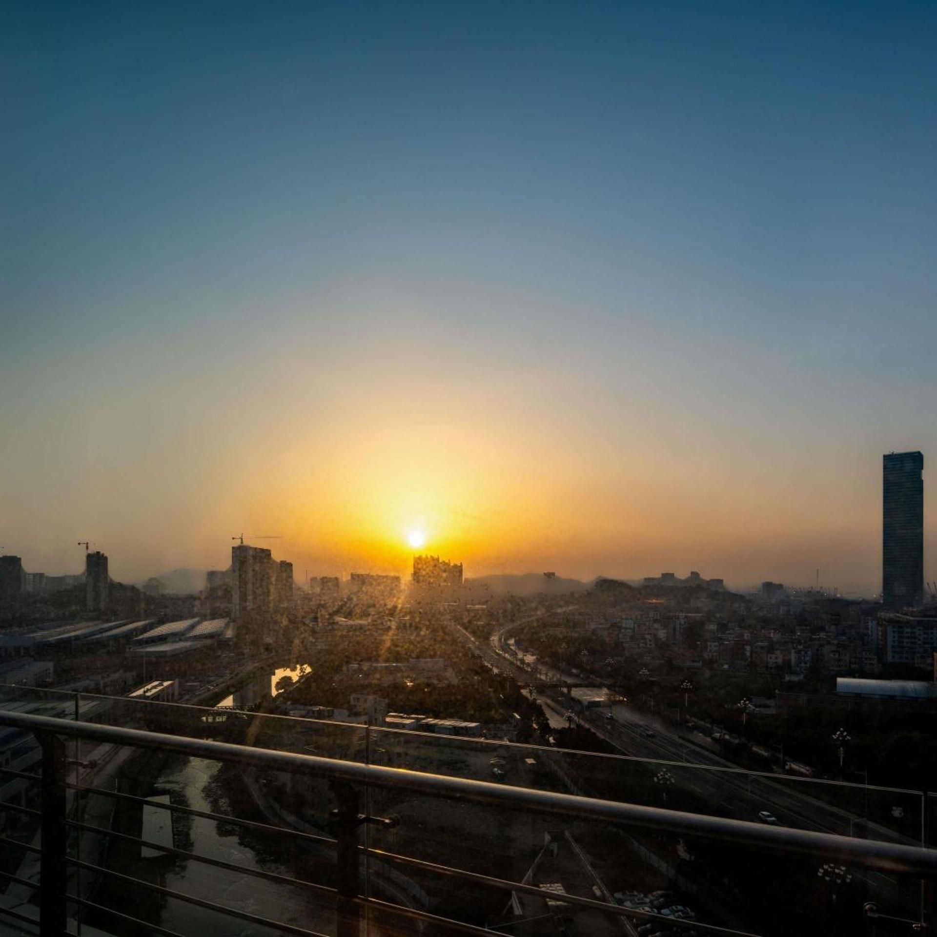 A cityscape at sunset with a clear sky, a prominent building on the right, and a bridge in the foreground.