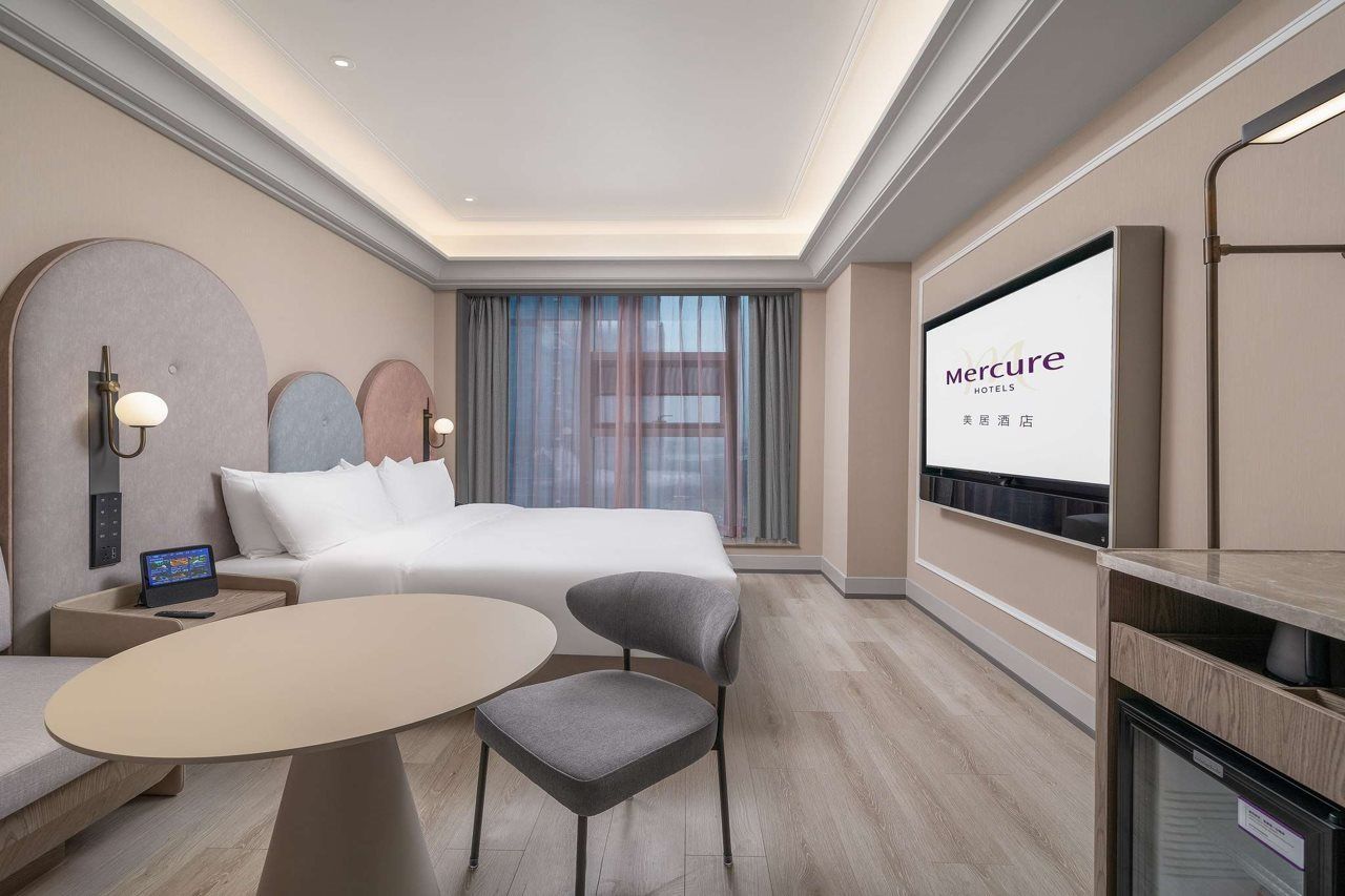 Une chambre d’hôtel comprenant un lit, un bureau avec un ordinateur portable, une télévision et un coin salon avec une table et des chaises.