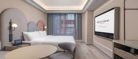 A hotel room with a bed, a desk with a laptop, a TV, and a seating area with a table and chairs.