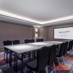 A conference room with a long table and chairs, a projector screen displaying 'Mercure Hotels', and a patterned carpet.