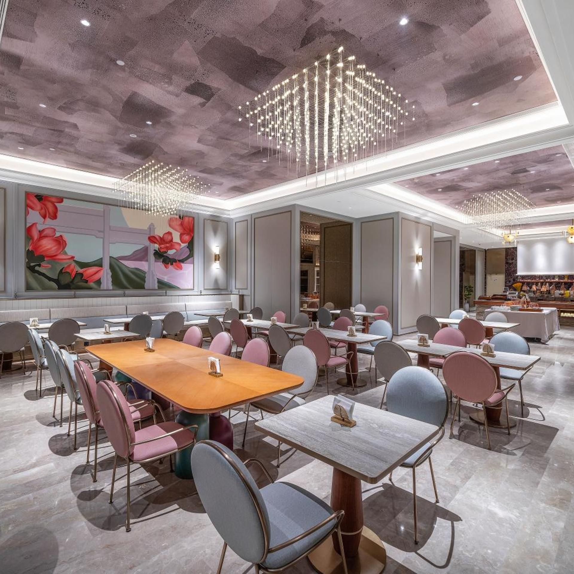 Un espace de restauration moderne, doté de plusieurs tables et chaises, d’une grande fresque florale et d’un lustre.