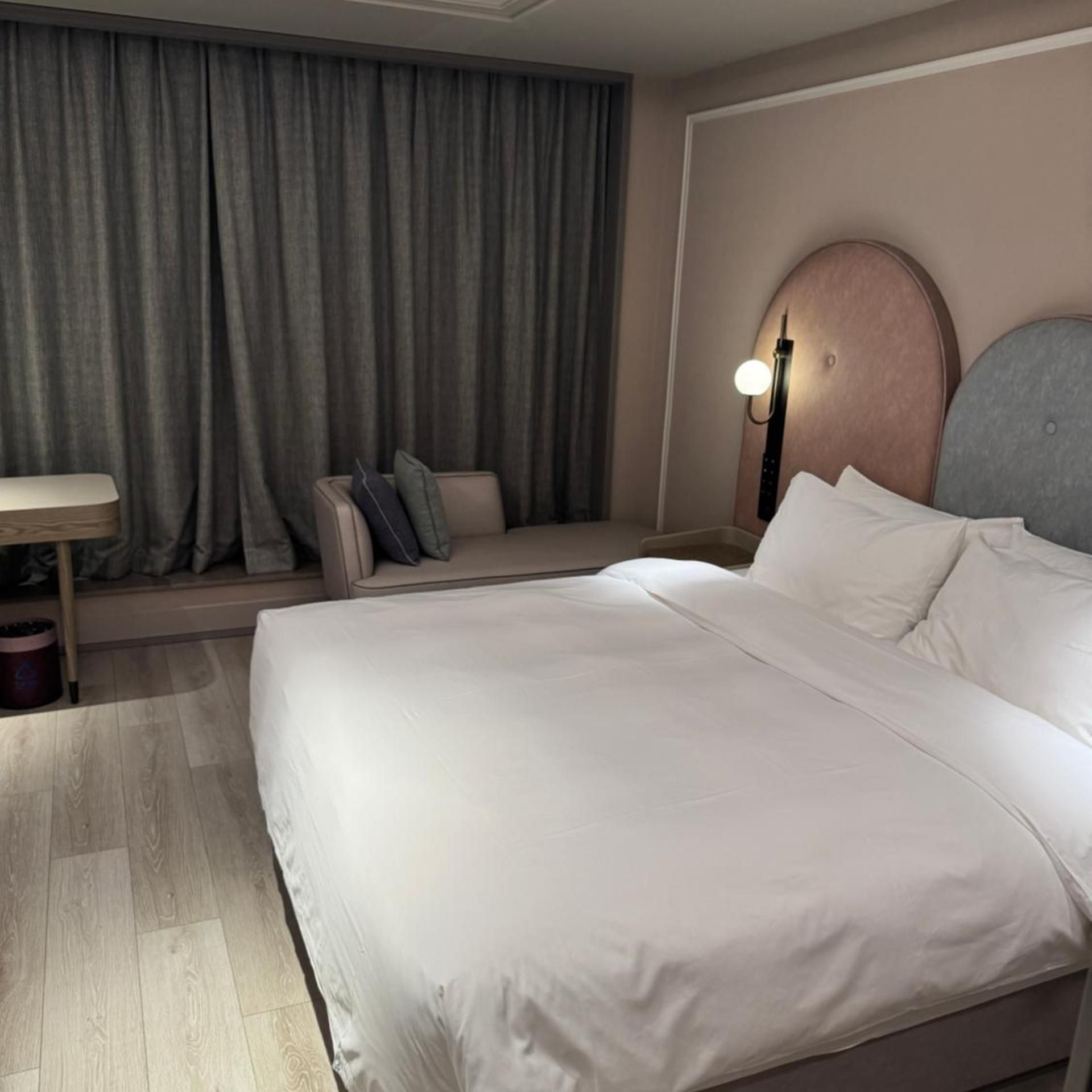 Une chambre d’hôtel avec un grand lit, une table de chevet, une lampe et une fenêtre avec des rideaux.