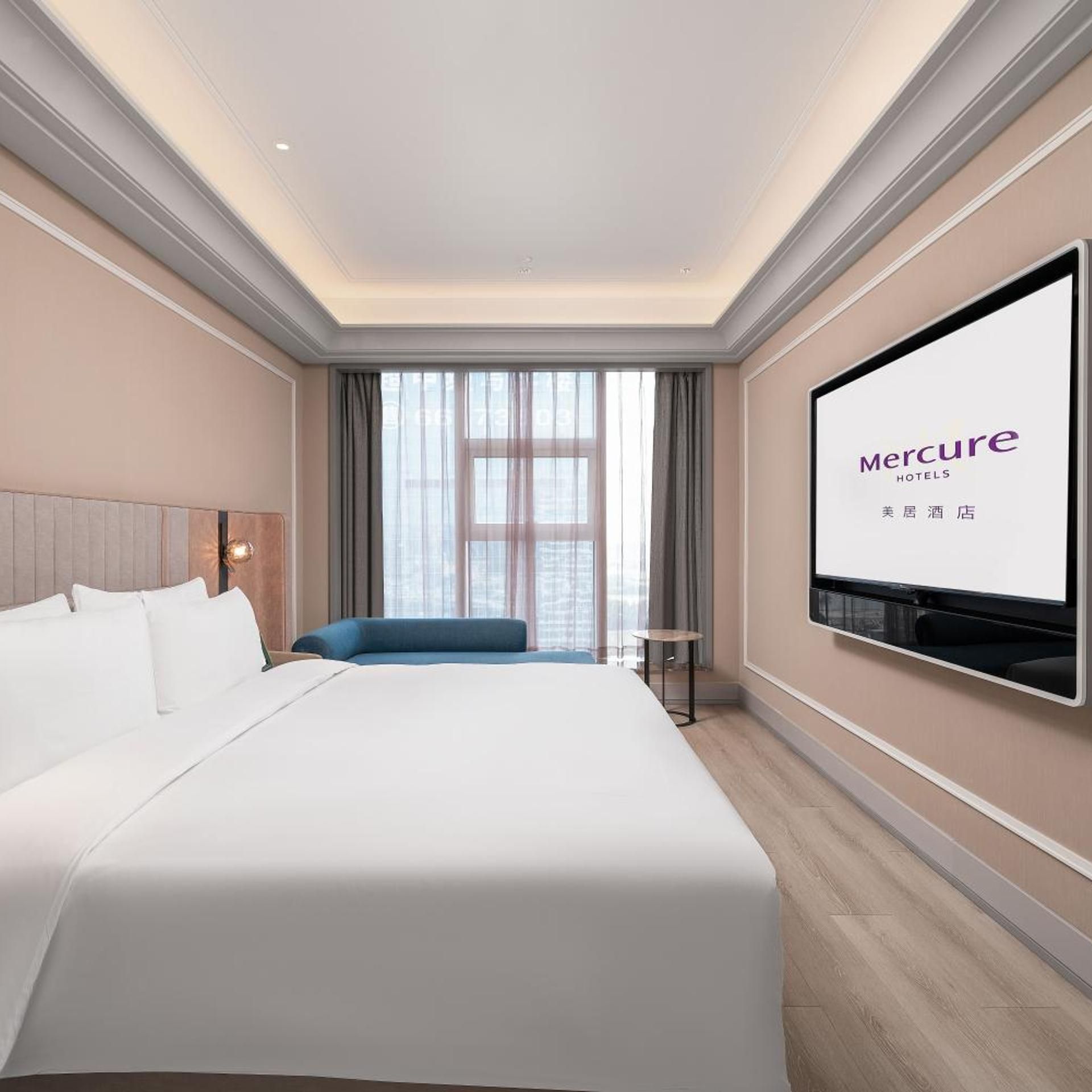 Une chambre d’hôtel avec un grand lit, un téléviseur fixé au mur et une vue sur la ville par la fenêtre.