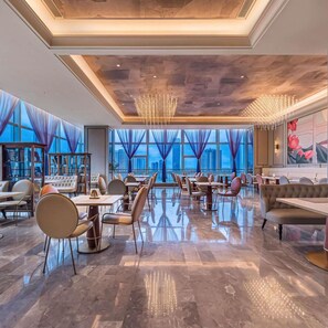 A spacious restaurant with high ceilings, modern chandeliers, and large windows offering a city view.