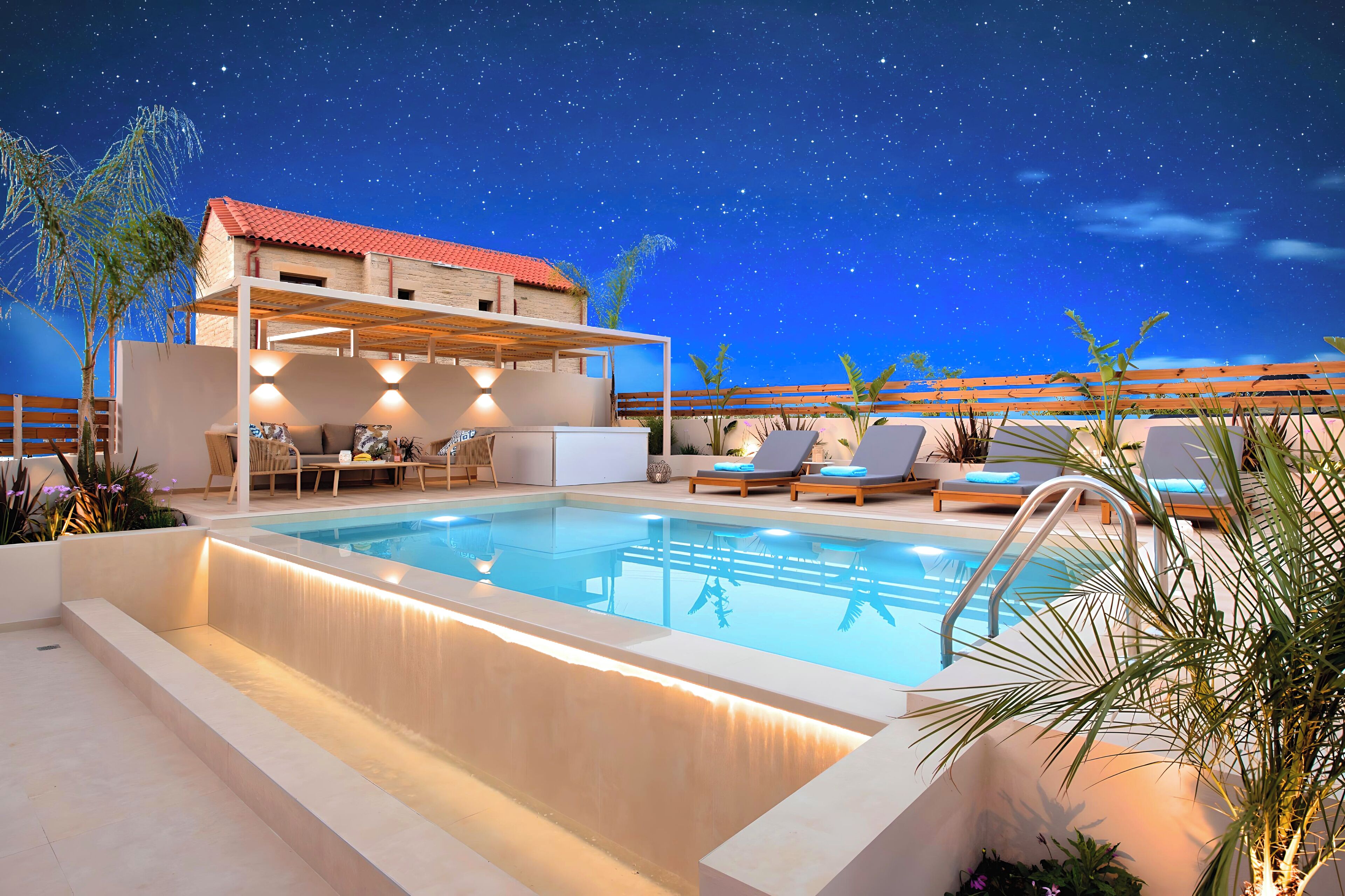 Piscina con vista al cielo nocturno, sillas de descanso y una zona de estar cubierta.