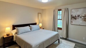 A bedroom with a bed, nightstands, a lamp, a window with curtains, and a painting on the wall. - Forks Cedar House (Forks)