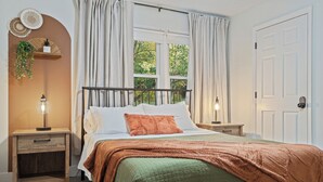 Un dormitorio con cama, mesita de noche, cortinas y puerta.