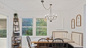 Un comedor con mesa de madera, dos sillas, un banco y una araña.