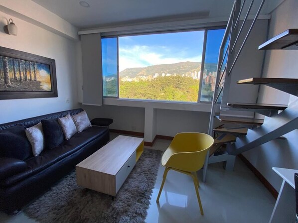 A modern living room with a sofa, a coffee table, a yellow chair, and a large window offering a city view. - Luxury Town Great Central View Duplex Coworking Tourist Area (Medellín)