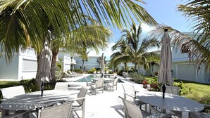 A poolside area with lounge chairs and umbrellas, surrounded by palm trees and a pool. - Treasure Cay, Palm Bay 7, Anchorage Drive (Treasure Cay)