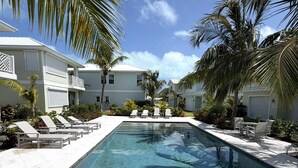 A swimming pool with lounge chairs, surrounded by palm trees and a clear blue sky. - Treasure Cay, Palm Bay 7, Anchorage Drive (Treasure Cay)