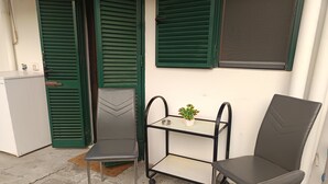 Un petit espace extérieur aménagé avec deux chaises et une petite table, une plante en pot et un réfrigérateur blanc.
