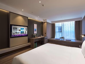 Habitación de hotel con cama, escritorio, televisión, ventana con cortinas y vista a la ciudad.