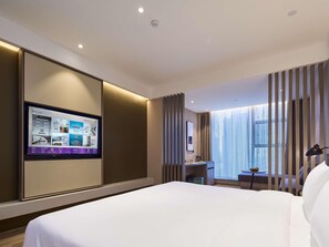 Ein modernes Hotelzimmer mit einem großen Bett, einem Schreibtisch und einem Fernseher, der die Annehmlichkeiten des Zimmers zeigt.