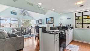 A modern kitchen with a central island, a dining area with a sofa and chairs, and a living room with a couch and a coffee table. - Beach Life, Heated Pool, Hot Tub, Close to Beach (Myrtle Beach)