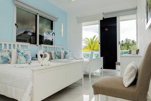 Relax in a serene space with a large bed, comfortable armchair, and expansive window views of palm trees.
