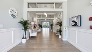 A hotel lobby with a central seating area, potted plants, and a signboard. - Your Perfect Vacation Townhome Just Steps from the Sand! - Full Amenities (Fort Pierce)