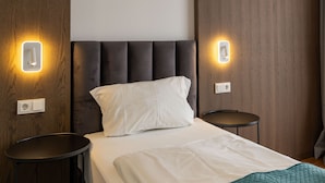 Habitació d'hotel moderna amb un llit gran, dues taules de nit i un panell de capçal amb il·luminació integrada.