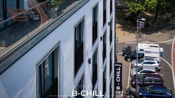 Hotel amb un disseny modern, amb un balcó de vidre i vista a una torre històrica al fons.
