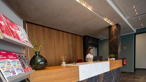 Taulell de recepció amb superfície de marbre, panells de fusta i un arranjament floral amb plantes verdes.
