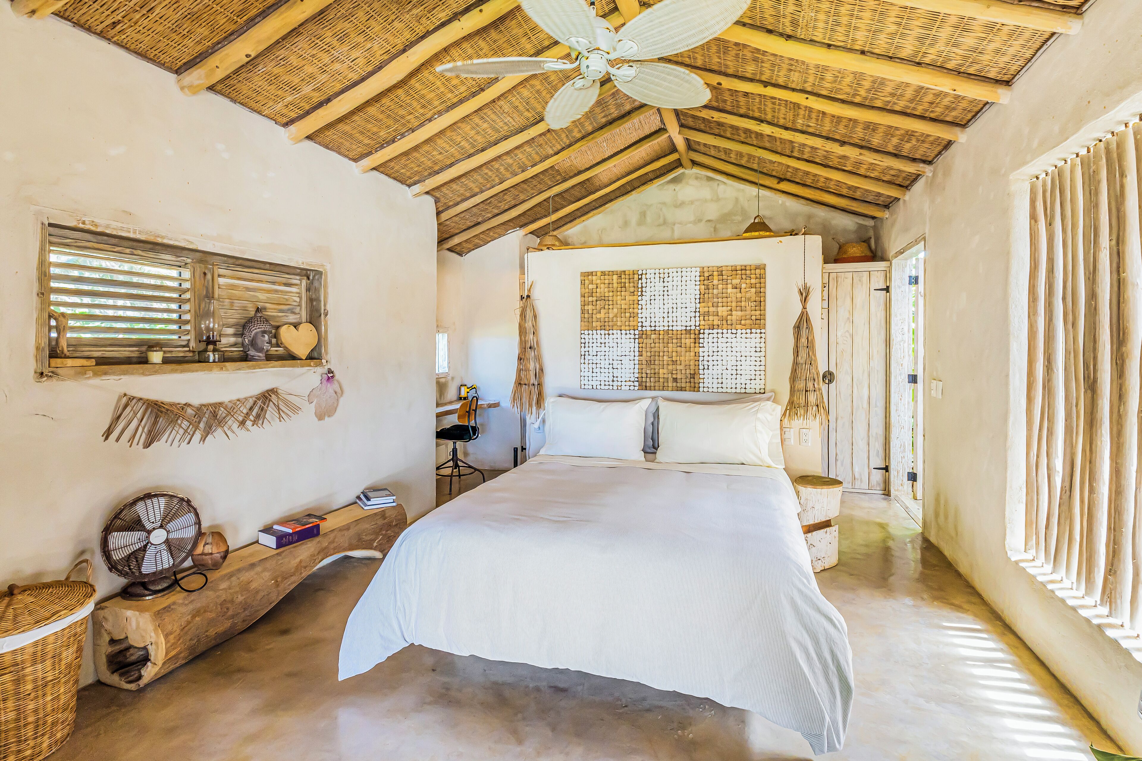 Quarto com cama grande, ventoinha no teto, janela com persianas e um painel de parede tecido.