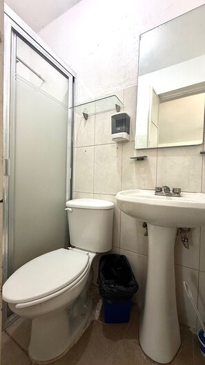 Un baño pequeño con inodoro, lavamanos y cabina de ducha de vidrio.