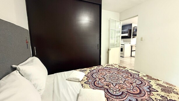 Una camera d'hotel con un letto, una porta scura, un tappeto a motivi e vista sulla cucina.
