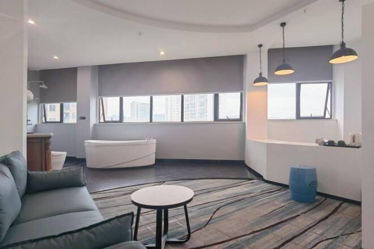 A modern living room with a sofa, a round table, a bathtub, and large windows.
