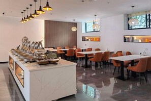 A modern dining area with a buffet setup, multiple tables, and chairs. - Jinglan Yipin Hotel (Jingdezhen Taoxichuan Branch) (Jingdezhen)