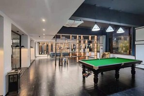 A billiards room with a pool table, shelves with sports equipment, and a view of the city. - Jinglan Yipin Hotel (Jingdezhen Taoxichuan Branch) (Jingdezhen)