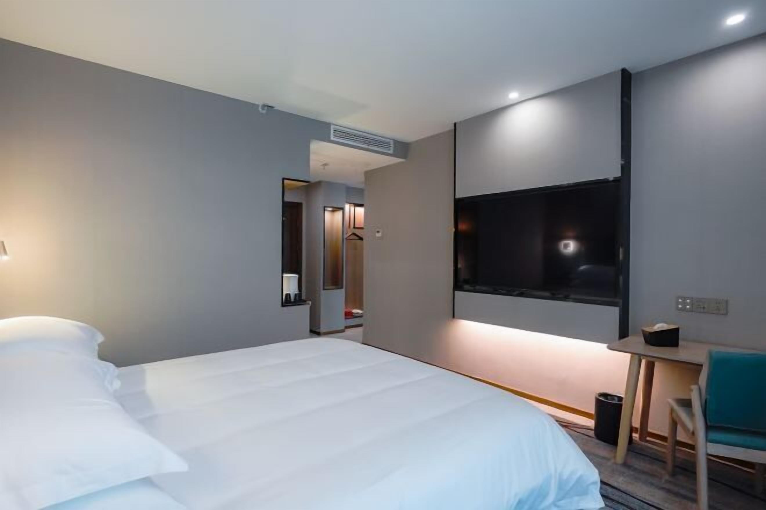 Quarto de hotel moderno com uma cama grande, uma TV fixada na parede e uma pequena escrivaninha com uma cadeira.