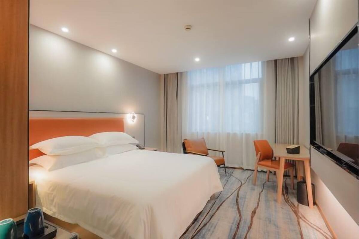 A hotel room with a bed, a desk, a chair, a TV, and a window with curtains.
