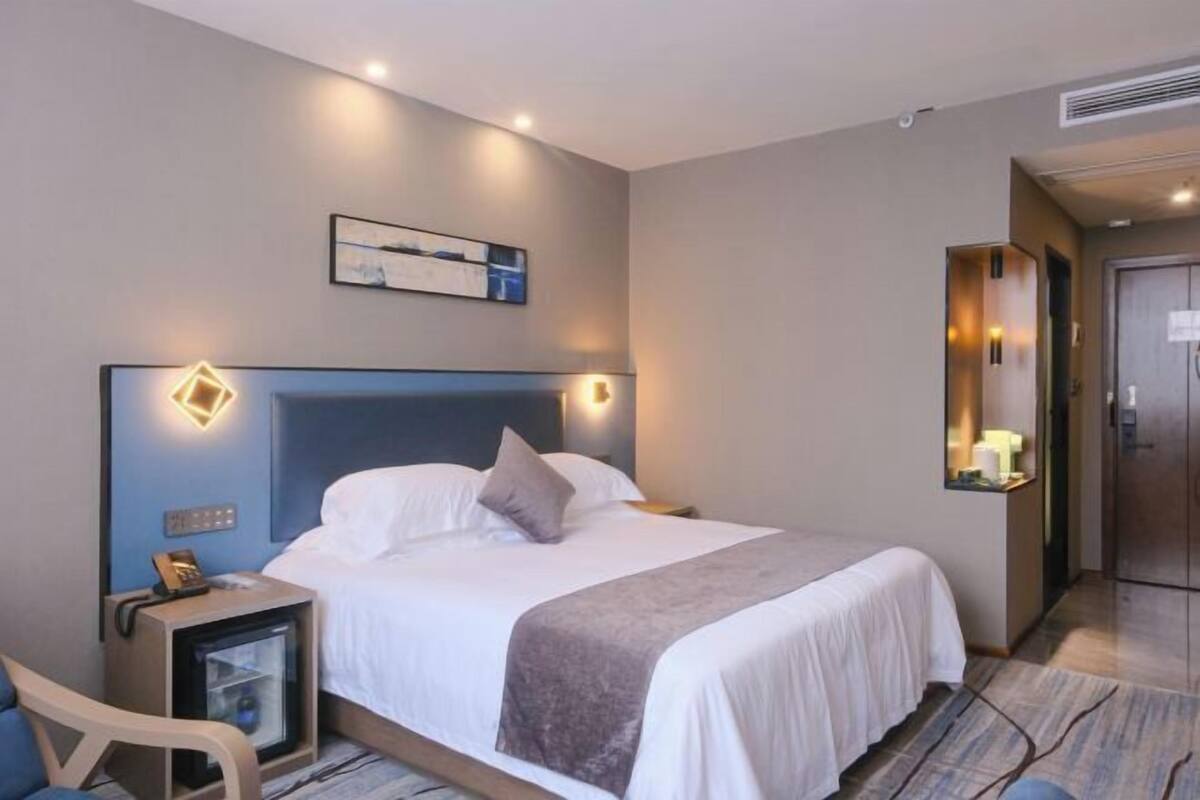 A hotel room with a bed, bedside table, chair, and a desk with a computer.