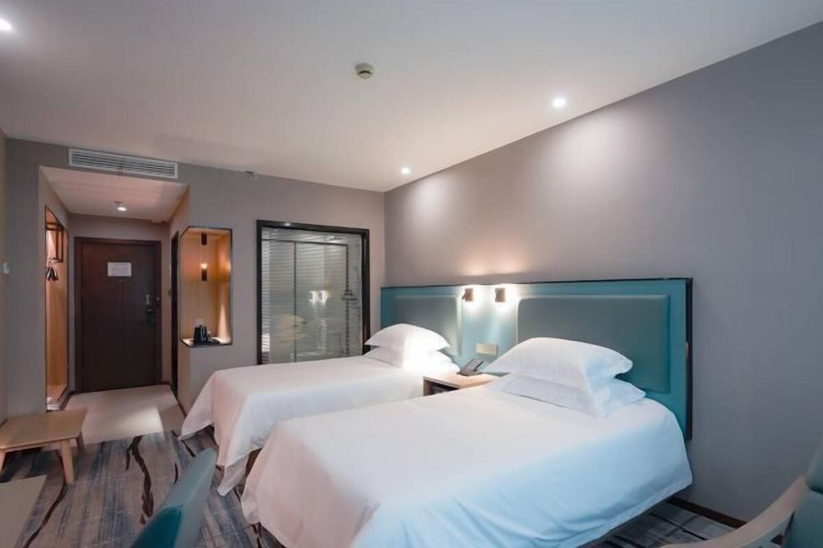 A hotel room with two single beds, a small desk, and a chair.