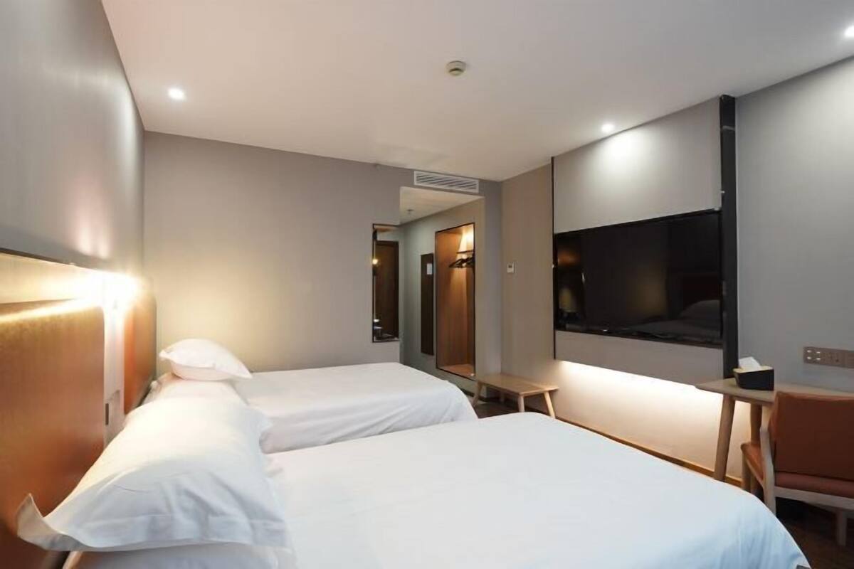 A hotel room with two beds, a TV, a small table, and a mirror.